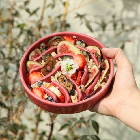 Hand holding a pink bowl filled with a colorful salad against a natural background