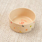 Beige pet bowl with colorful designs on a beige carpet