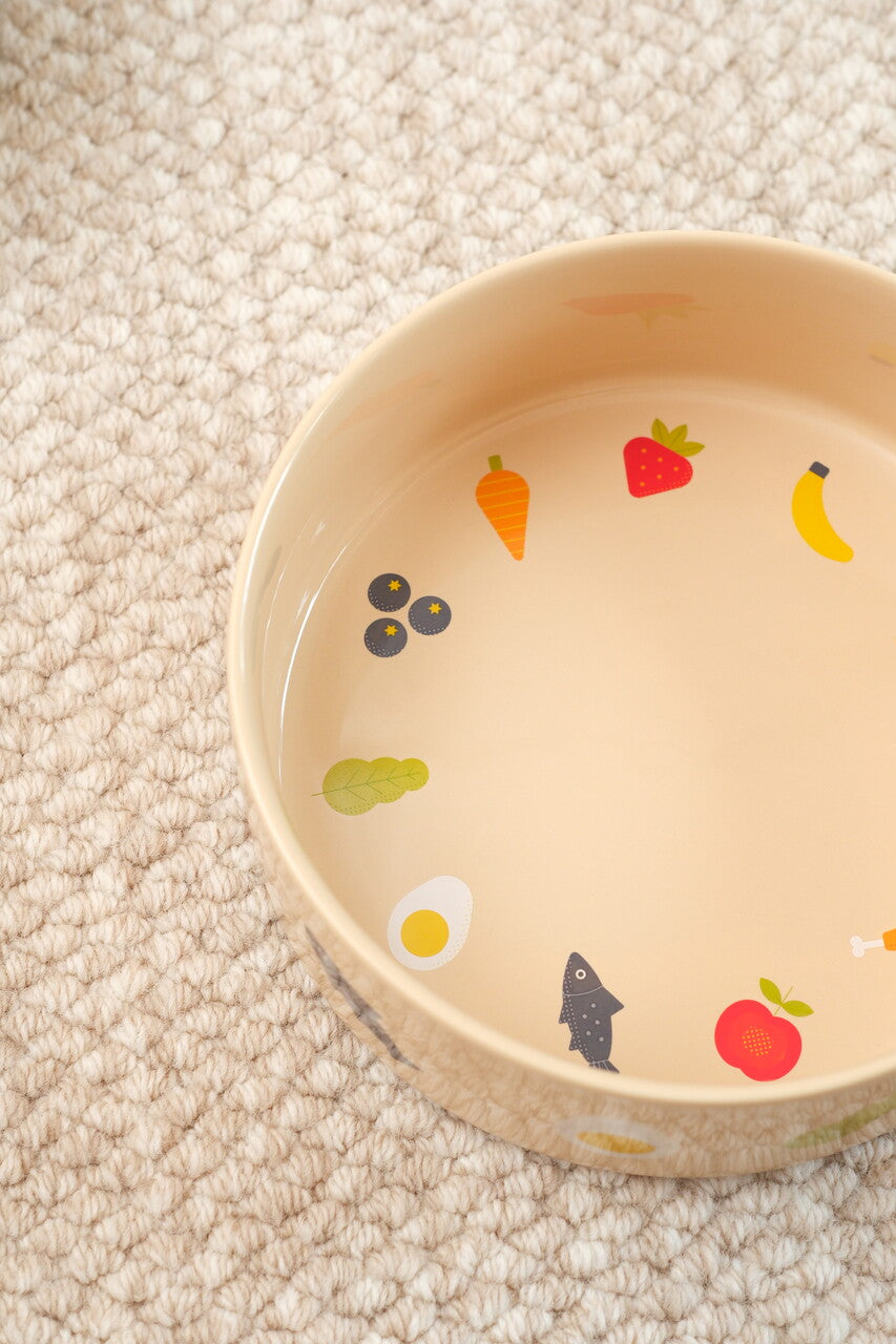 Beige ceramic bowl with fruit and vegetable patterns on a beige carpet